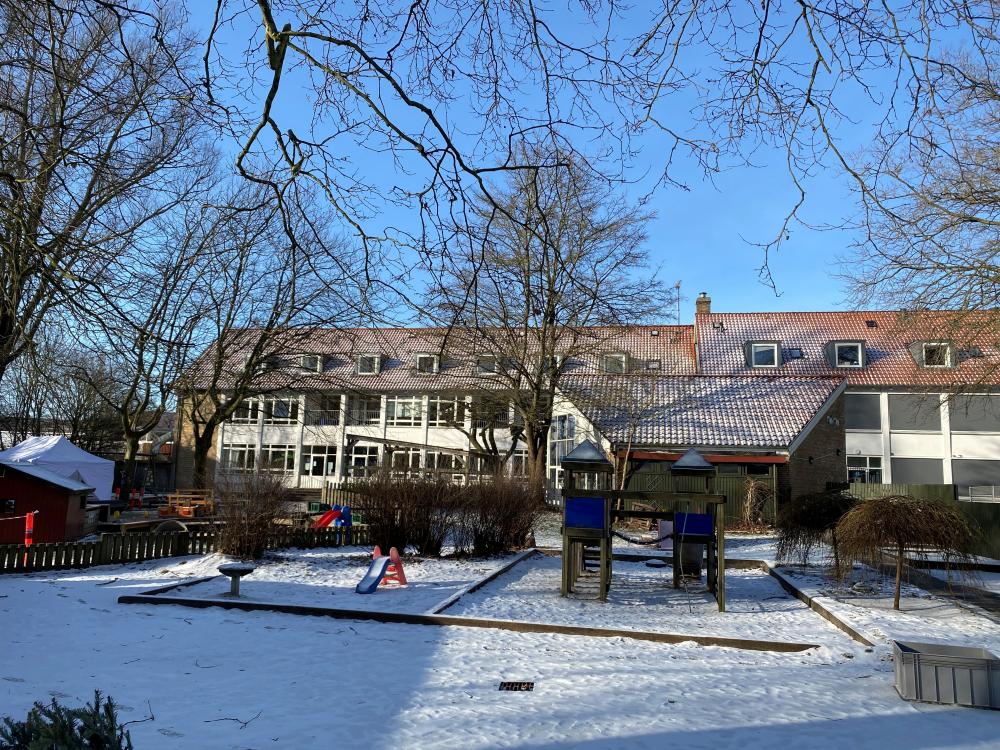 Vuggestuens legeplads på en flot vinterdag, med Børnehuset Carlshøj i baggrunden 